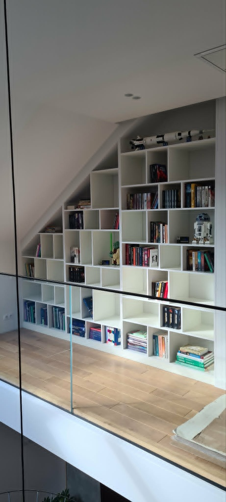 Biała biblioteczka na wymiar wpasowana pod skos, wypełniona książkami